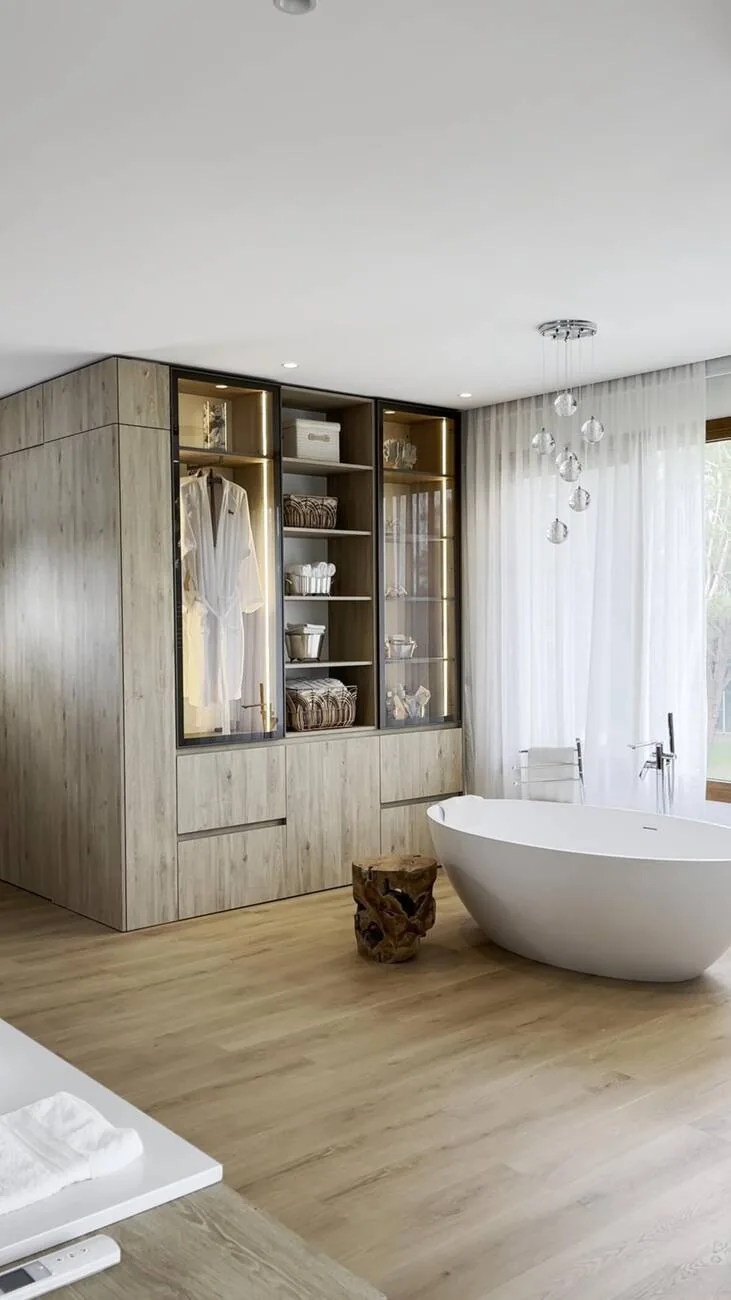 Auxiliar de ba&ntilde;o con m&oacute;dulos iluminados y frentes de vidrio, junto a la ba&ntilde;era